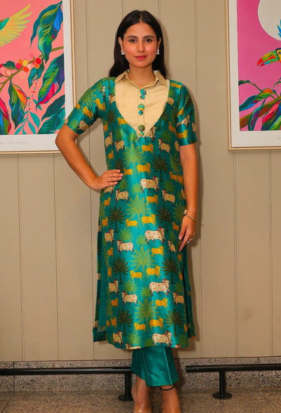 the Kriti Kavya tunic kurti set from Destiny by Anjali. This designer tunic set, crafted from lustrous mango silk fabric in a vibrant green shade, features delicate prints of cows, trees, and bushes inspired by the Madhuvan theme. The shining silk fabric makes it a trending choice for every season, offering comfort and style for all-weather wear. Ideal for festive events or casual outings, this occasion wear kurti set is perfect for all occasions, combining traditional charm with modern flair. Elevate your 