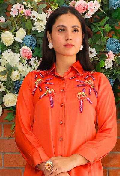 the Shimmer Glimpse coord set from Destiny by Anjali. This vibrant designer western wear comes in a striking bright orange, made from premium bombarg satin fabric. The shirt features intricate zardozi hand embroidery work, adding a touch of regal elegance. Fully lined for comfort, this set is perfect for all-weather and occasion wear, blending traditional craftsmanship with a modern aesthetic. Stay ahead of the trending fashion curve with this sophisticated and versatile floral coord set